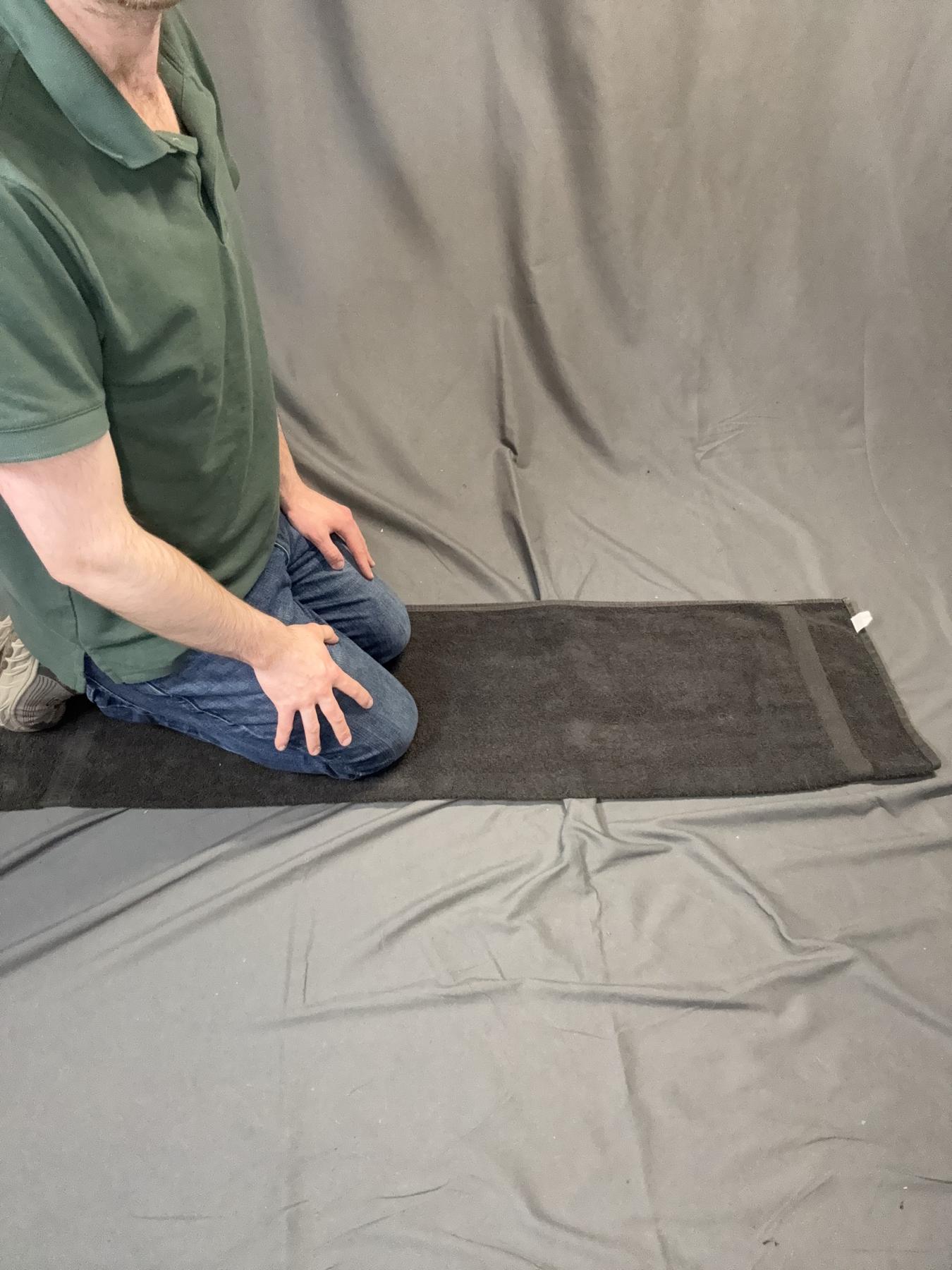 A player kneeling at the end of the folded towel to begin rolling.