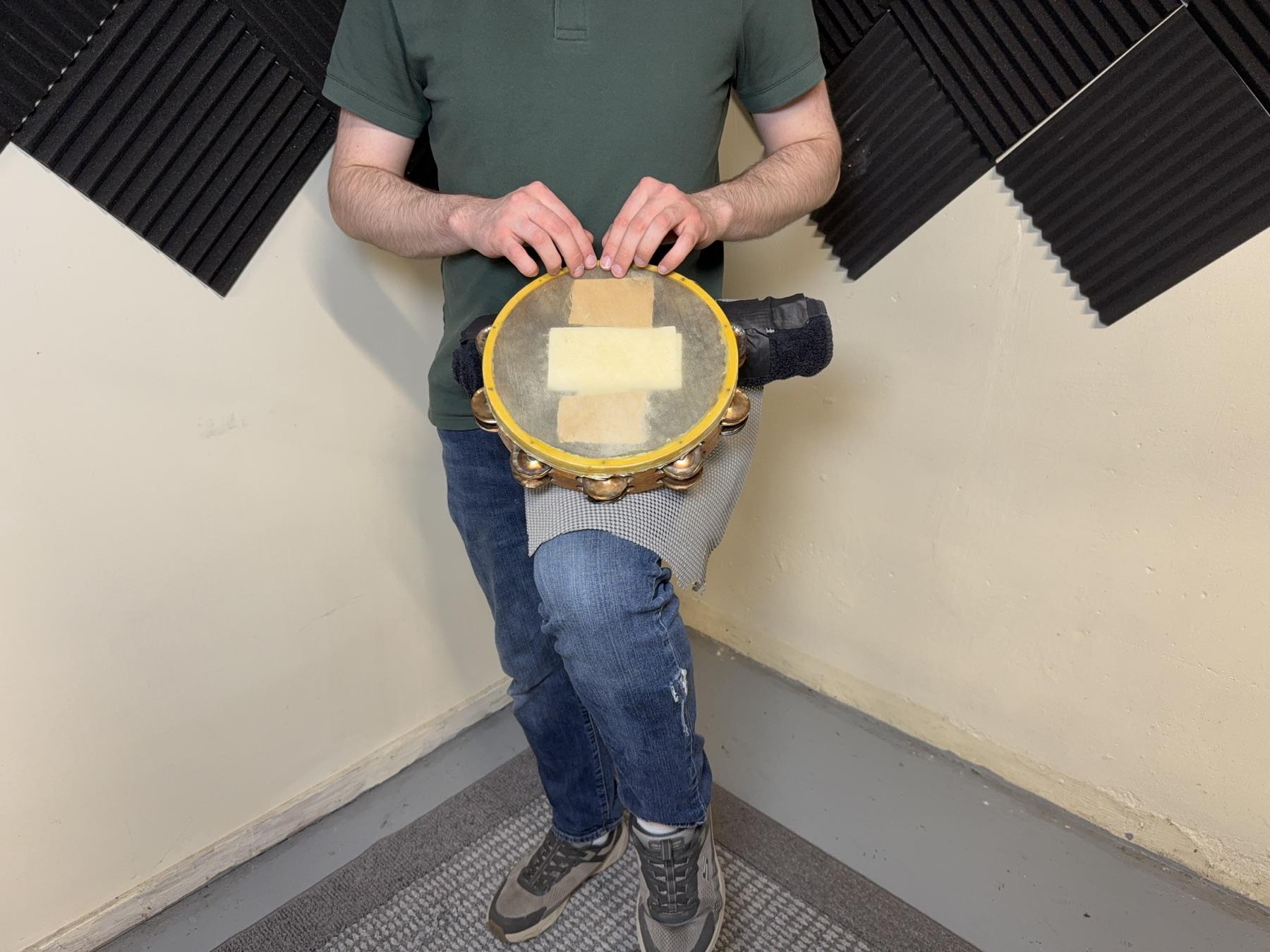 A player using fingers on a tambourine supported by a TAM-BURRITO.